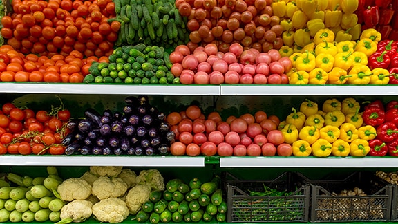 Different kinds of vegetables like bell peppers, tomatoes, egg plants, and cauliflower organized in a vegetable market