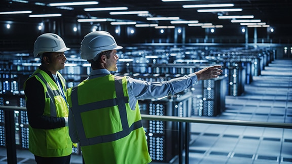 Two technicians standing inside a large industrial plant where one of them is pointing to something on the right side and talking