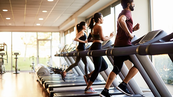 A man and two women running on treadmills in a gym 