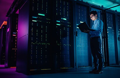 A man working on his laptop in a dimly lit server room