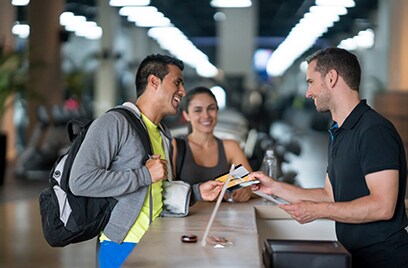 A man and a women smiling and talking to the receptionist at a gym