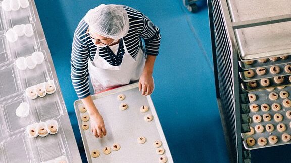 A worker at a bakery taking tarts from a trolley and placing them in boxes