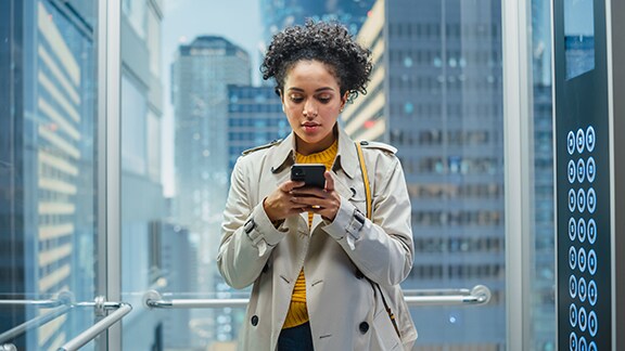 A woman looking at her phone while in a lift with transparent glass walls