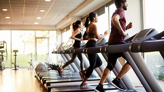 A man and two women running on treadmills in a gym