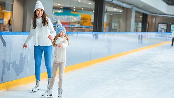 A mother and daughter ice skating in an indoor ice rink