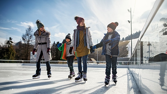 A group of four kids skating in an outdoor ice rink