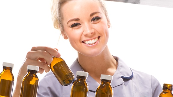 A smiling women holding a medicine bottle and several other bottles in front of her