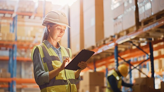 A female working standing inside a warehouse and looking at her tablet