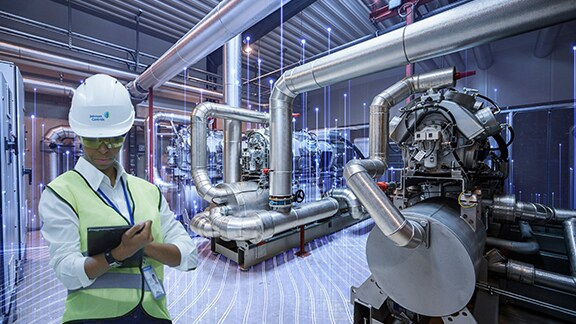 A man wearing safety jacket and helmet working on a tablet in a machine room